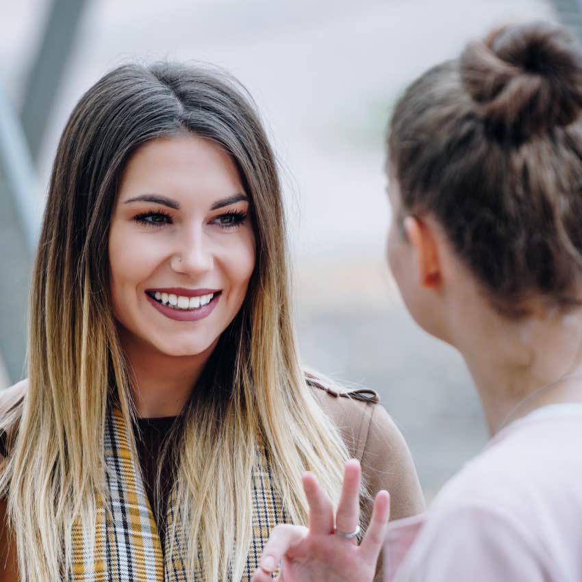 woman with long hair smiling with her friend okay hand sign