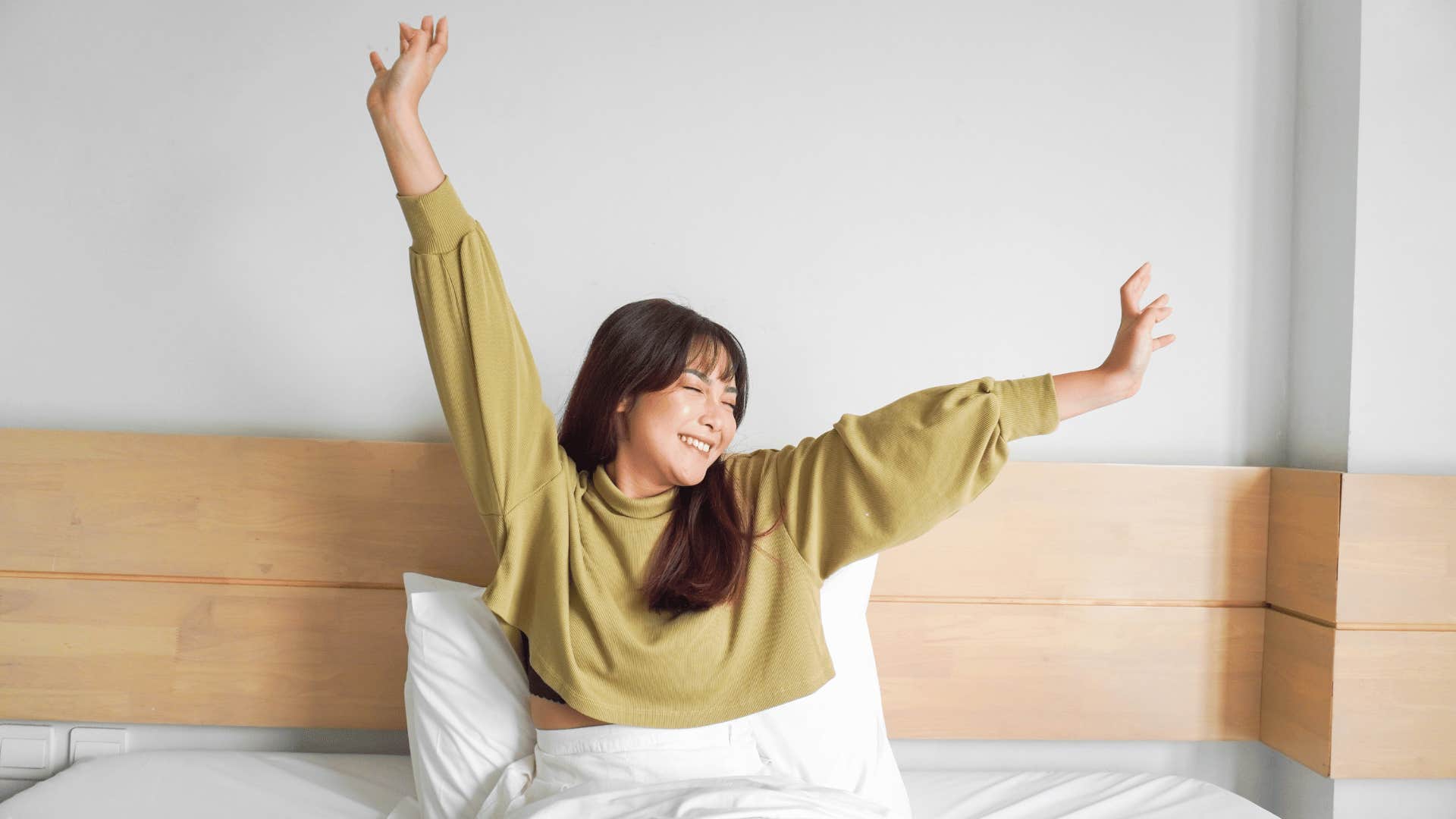 Happy woman stretches her arms after waking up