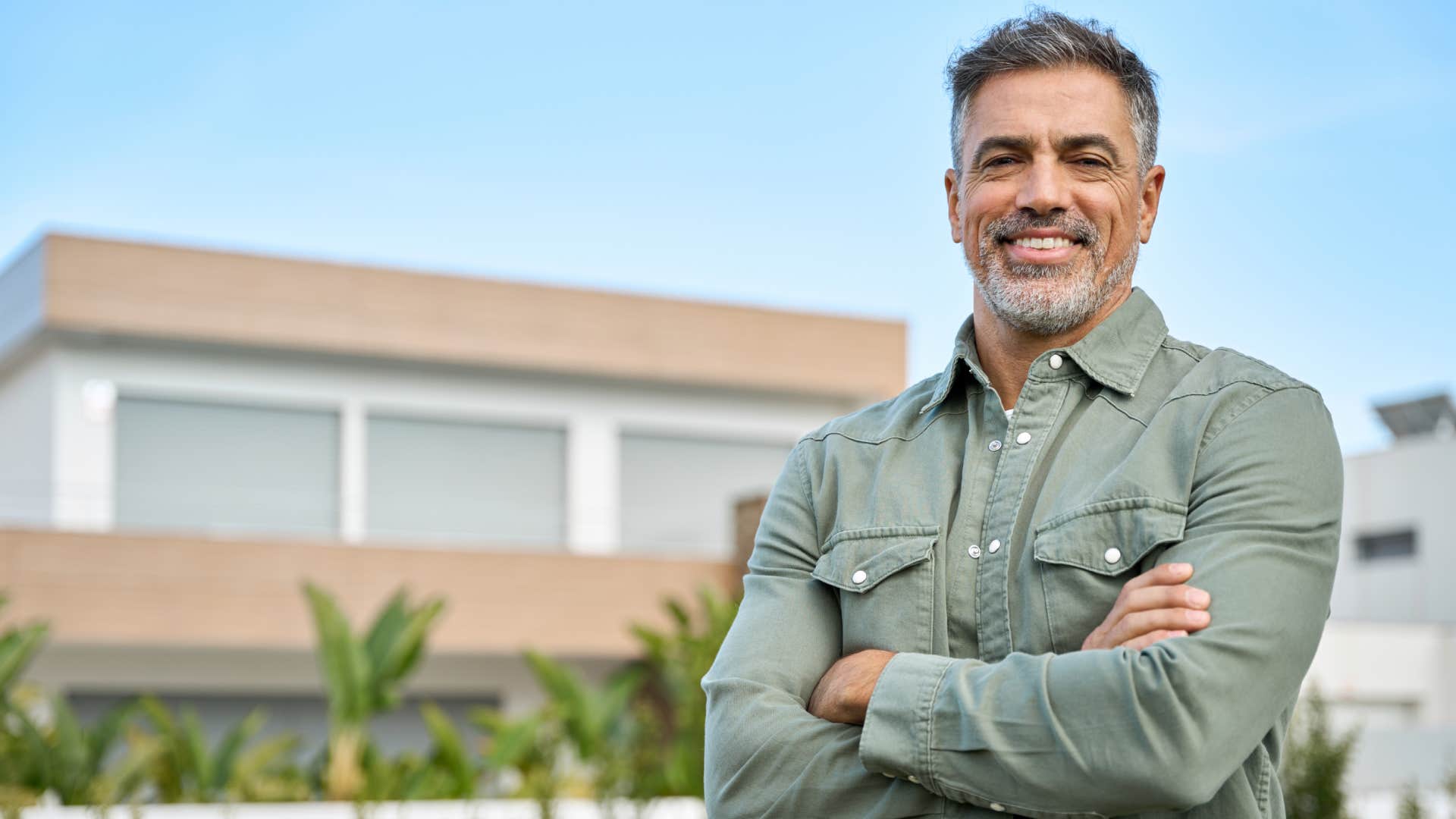 man standing with arms crossed in front of house