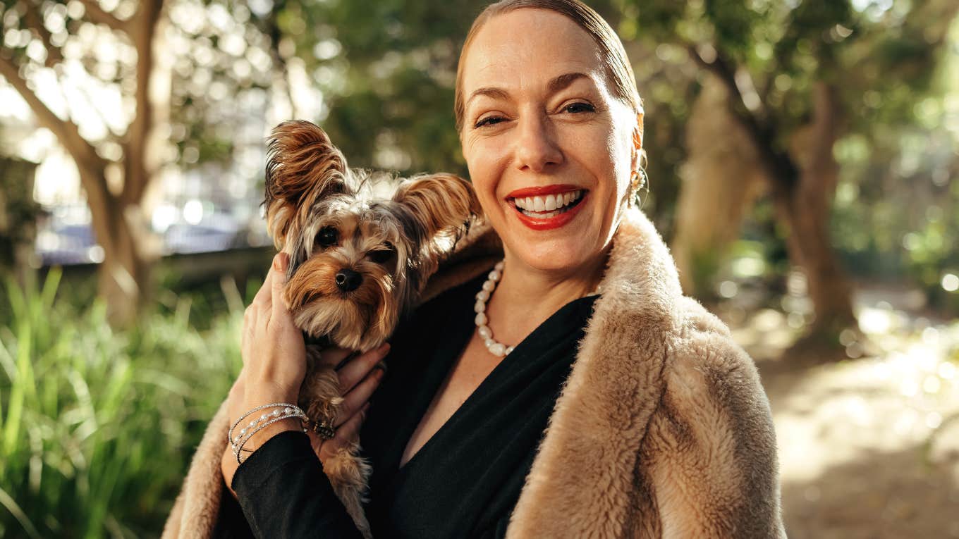 Fancy woman smiling outside and holding her small dog.