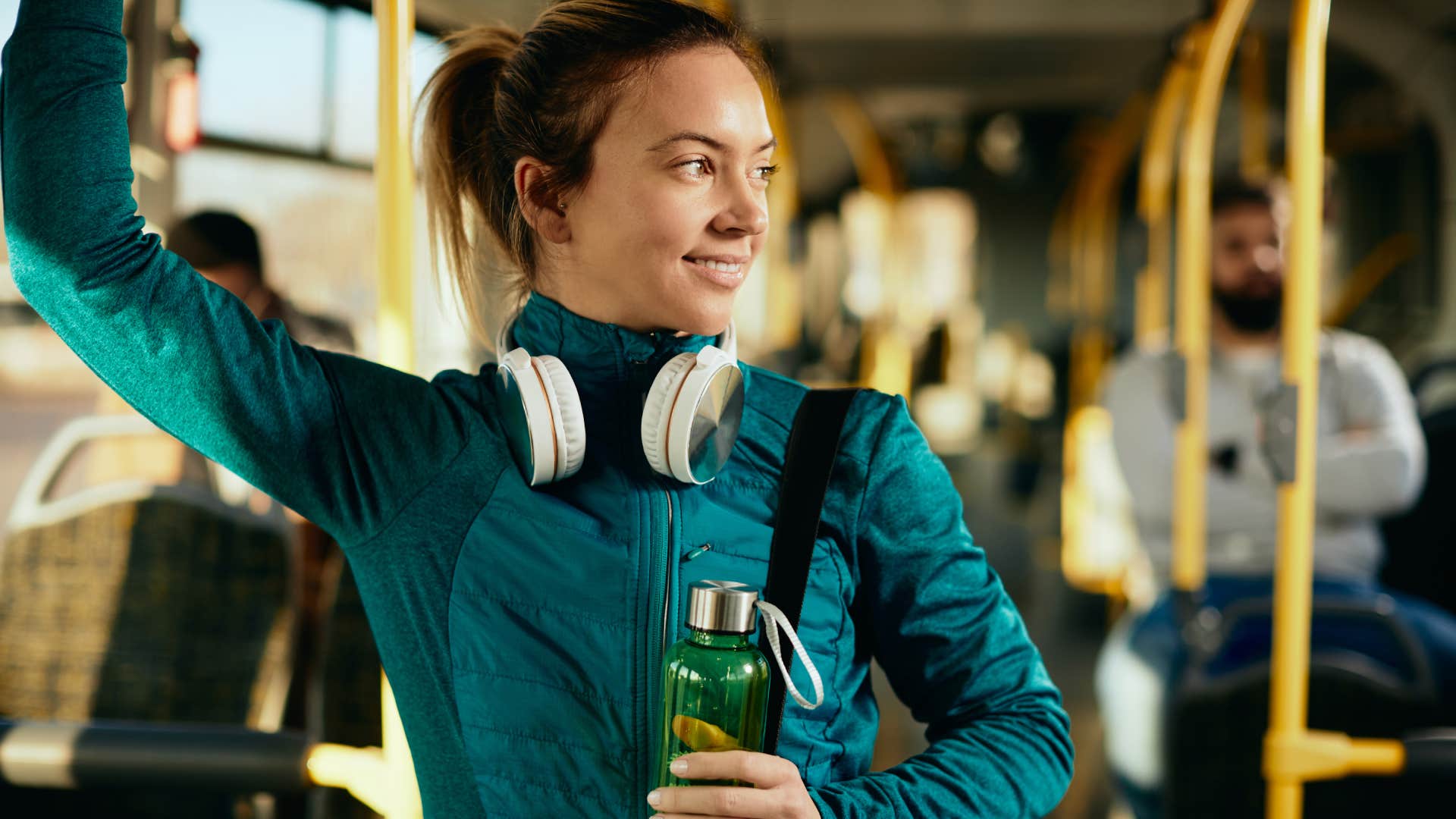 woman standing on bus holding a fancy water bottle