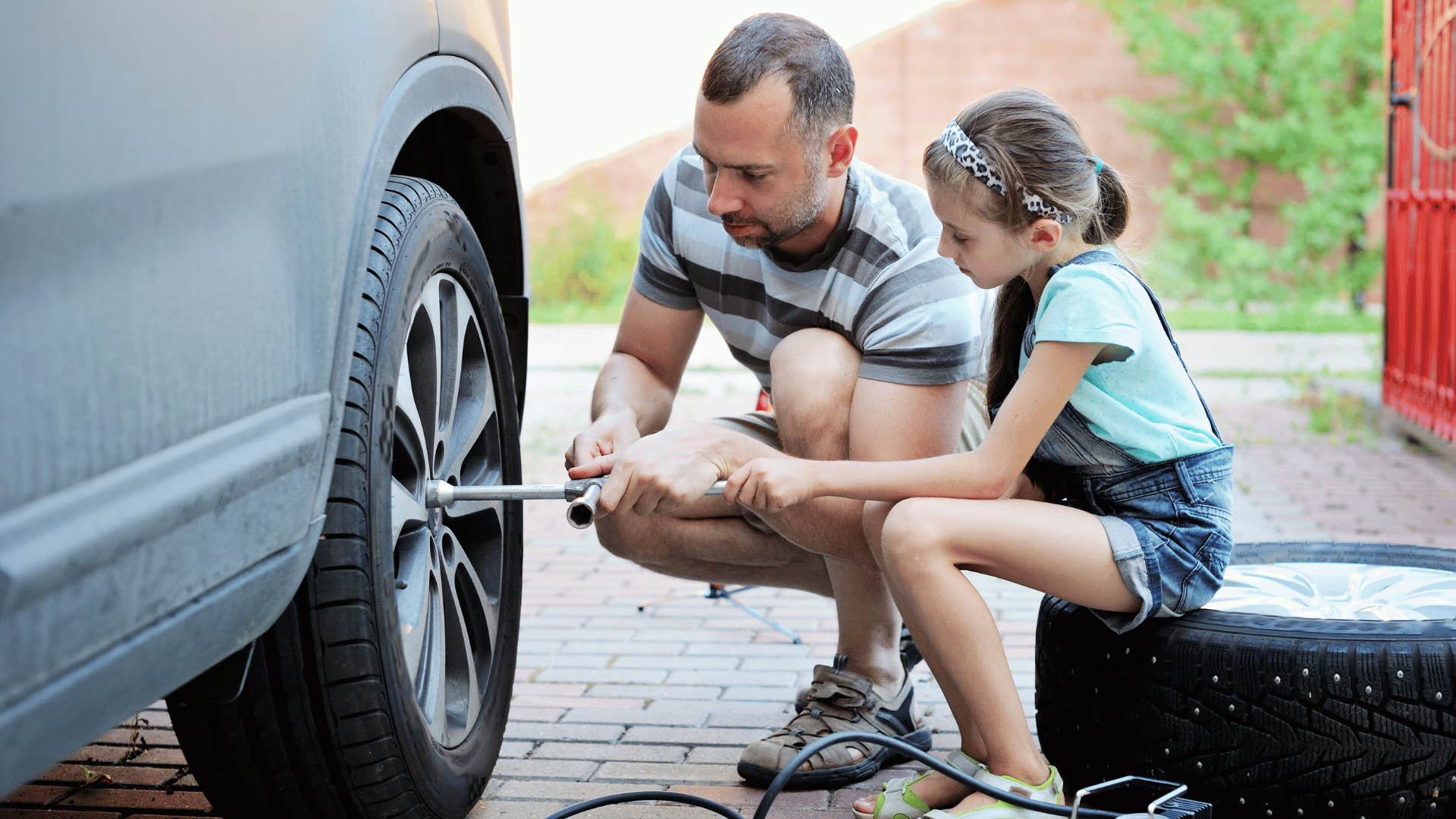 Father shows daughter how to change tire on car, neither know how to change a tire