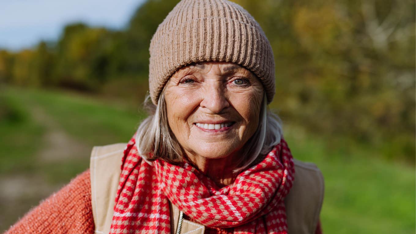 Boomer woman smiling at the camera outside.