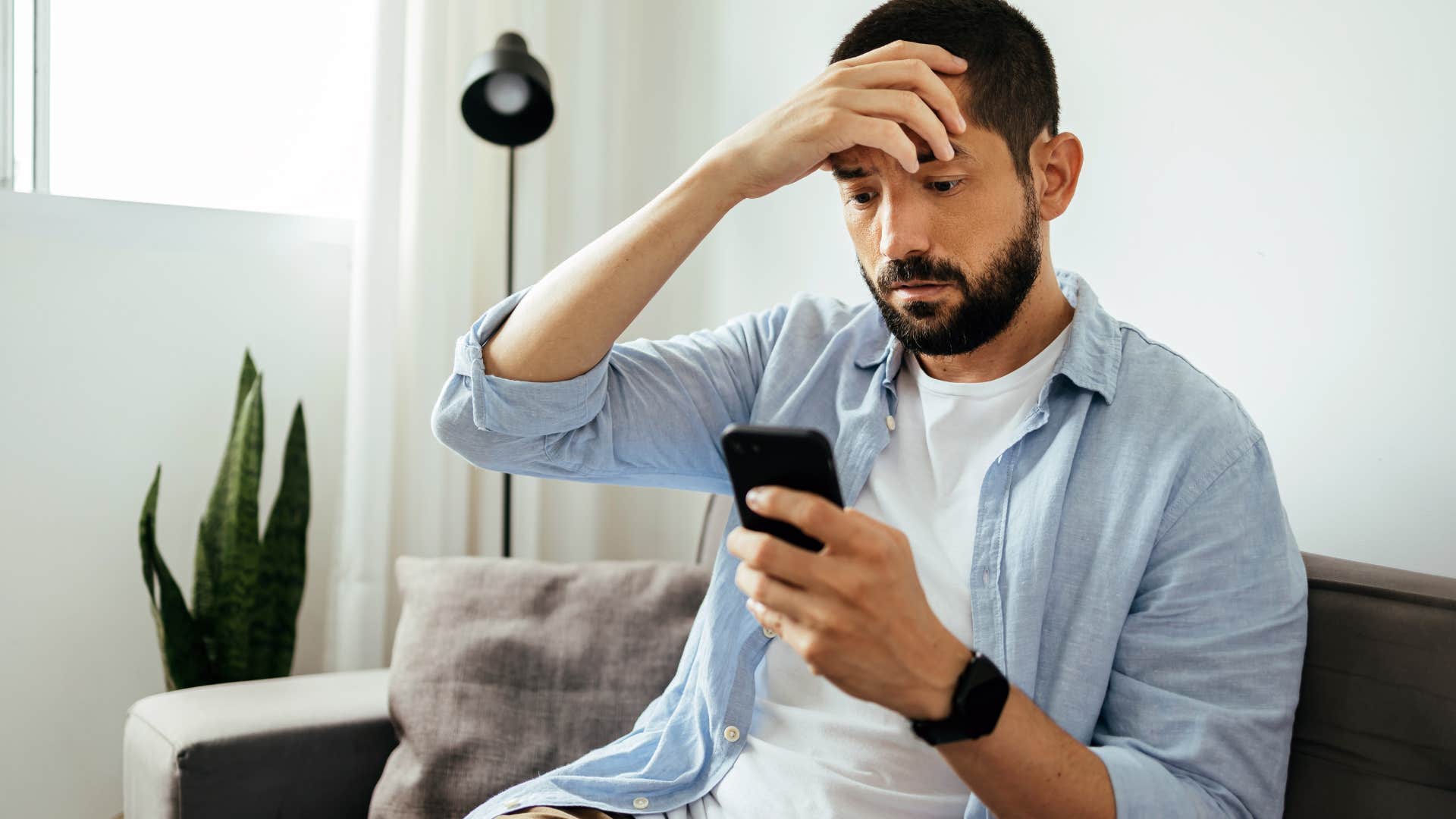 embarrassed man holding his forehead and looking at his phone