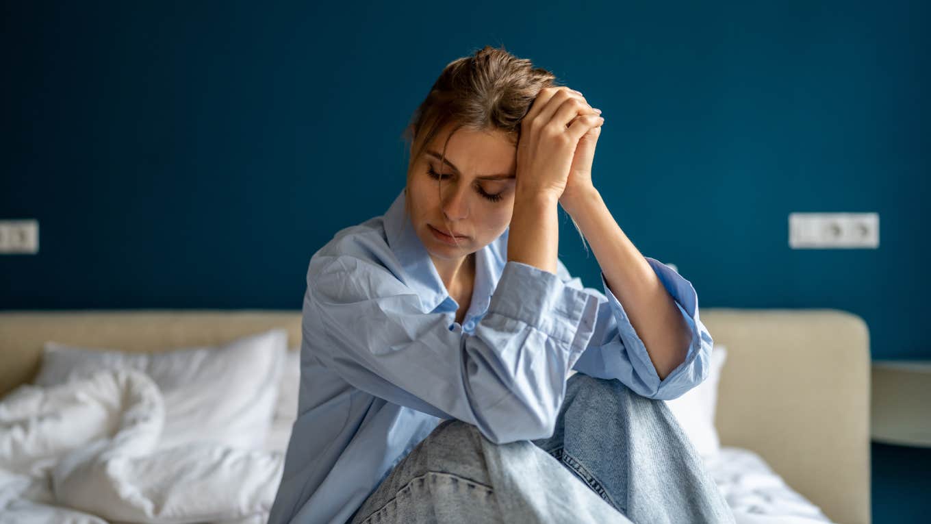 Woman Who Lives Paycheck To Paycheck Asks What’s The Point? depressed woman sitting on bed