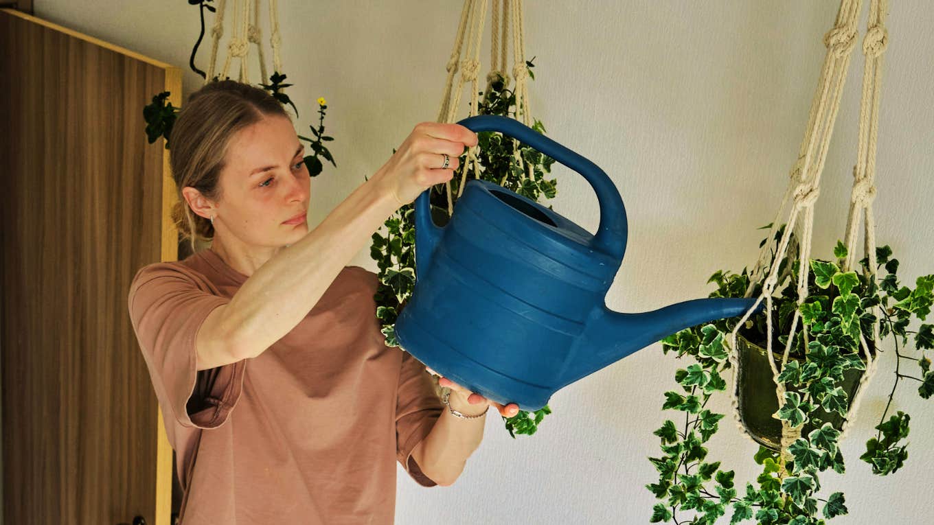 TK Everyday Objects That Transform The Energy In Your Home, According To Psychology Woman watering plants in her home, transforming energy.