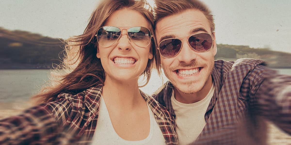 Funny curly male youngster and his girlfriend pose for making selfie  portrait against blurred nature background, have positive expressions.  Couple in love use modern cell phone for entertainment Stock Photo | Adobe