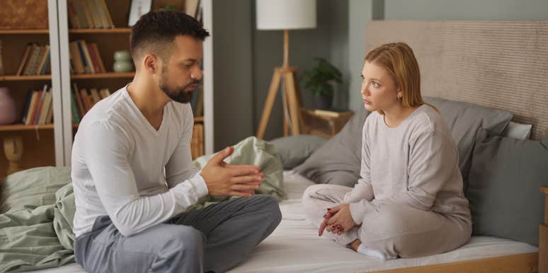 unhappy couple arguing while sitting on bed