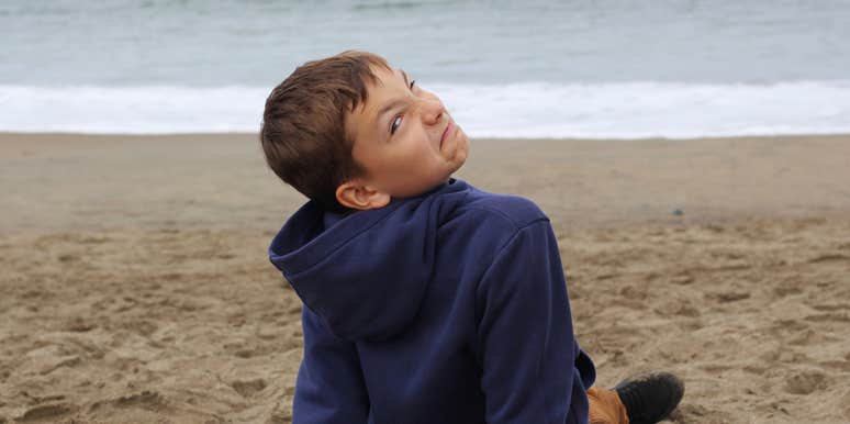 young boy making a face while sitting on the beach