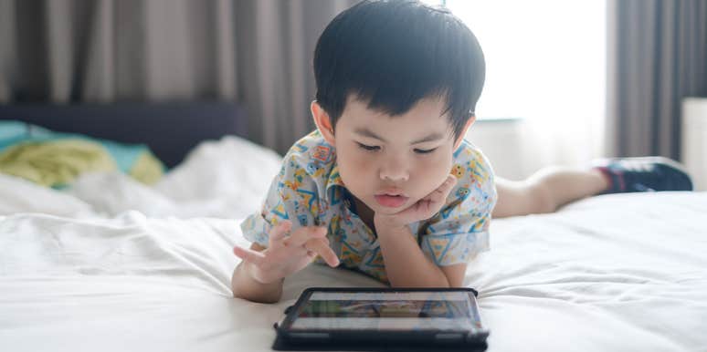 little boy lying on bed using tablet