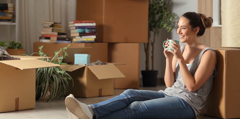 Happy tenant resting drinking coffee moving home sitting on the floor in the night