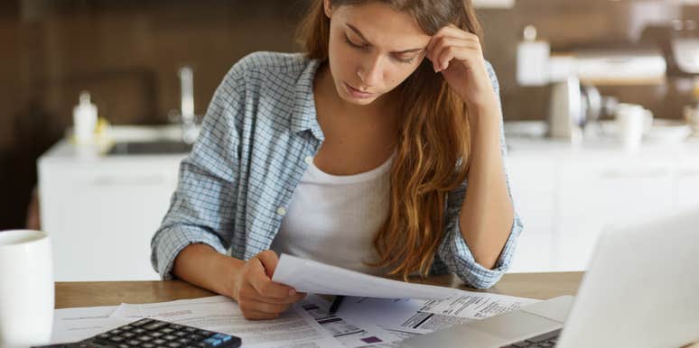 young woman with calculator, computer and bills spread out across table