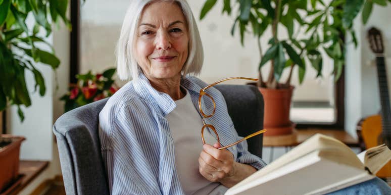 portrait of older woman holding glasses and reading book at home