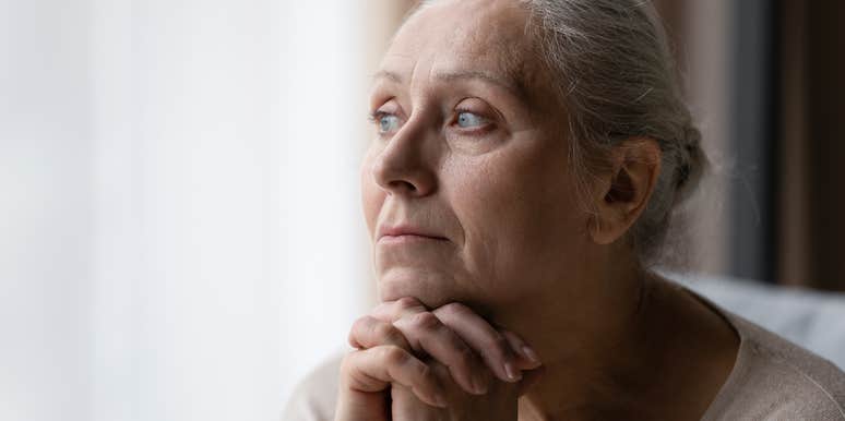 Older woman looking sad staring out a window.