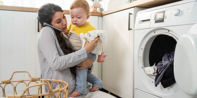 mom trying to do laundry while talking on the phone and holding toddler