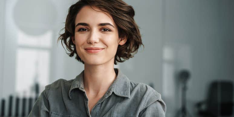 Image of young joyful woman smiling while working with laptop in office