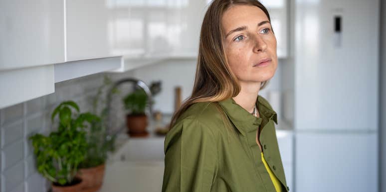 Pensive thoughtful woman with distressed mood stands in kitchen of home