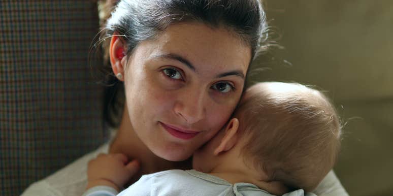 casual mom looking to camera holding sleeping infant