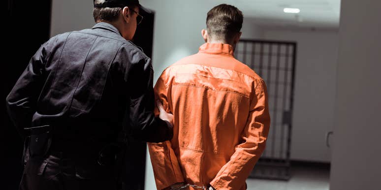 rear view of prison officer leading prisoner in handcuffs in corridor