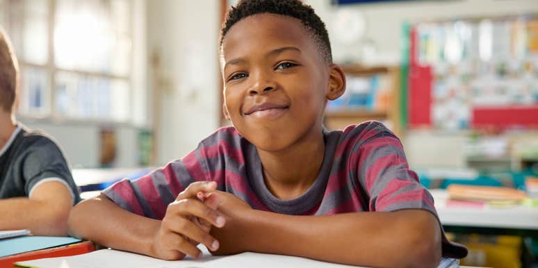 happy black elementary boy studying in classroom while looking at camera