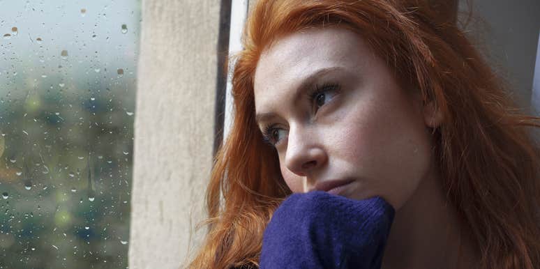 young woman looking sadly out a window