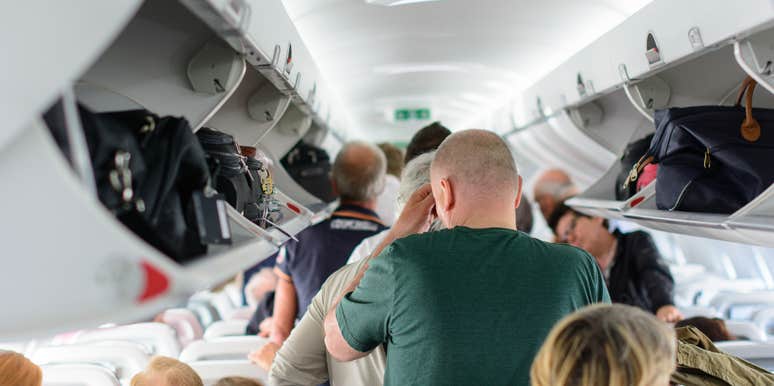 airline passengers standing and sitting while waiting to deplane