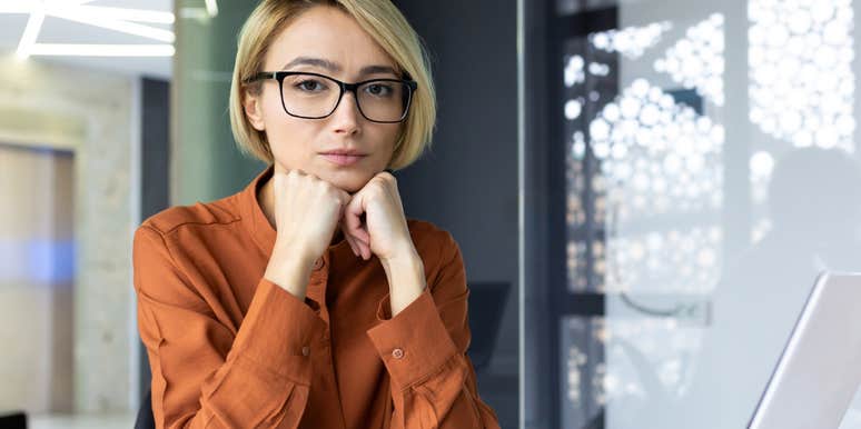 woman with hands under chin wearing glasses at work