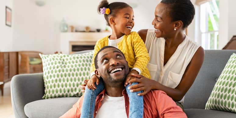 little girl sitting on dad's shoulders smiling at mom