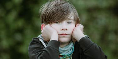 little boy looking sad while holding head in hands