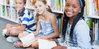 group of kids reading books on floor of library