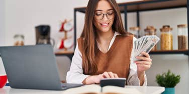  woman using laptop counting money at home