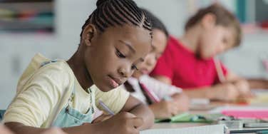black student writing in notebook while sitting in class