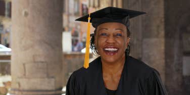 Portrait of senior black woman in graduation gown smiling and cheering