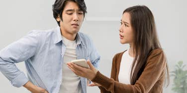 Man looks angrily at girlfriend's phone. 