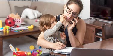 stressed mom working on laptop with toddler sitting on her lap