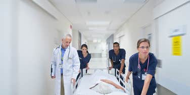 person being wheeled down a hospital hallway in bed by medical team
