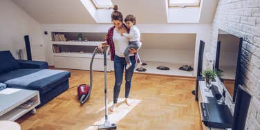 woman cleans and vacuums living room while holding boy in her arms