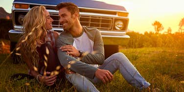 loving couple sitting in the grass in front of a car