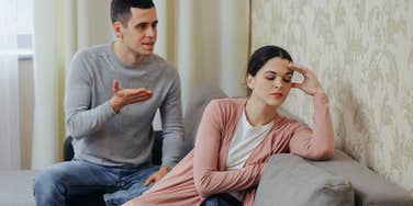 husband arguing with annoyed wife whose back is to him while sitting on couch