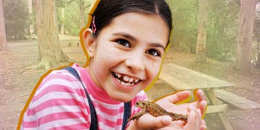 Young girl smiling holding a frog, reducing homesick anxiety at camp