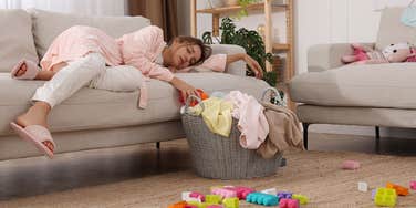 stressed woman laying on couch surrounded by toys and laundry