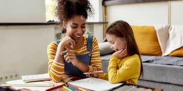 Babysitter sitting with young girl at a table. 