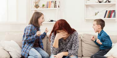 two kids fighting while tired, frustrated mom hangs her head between them