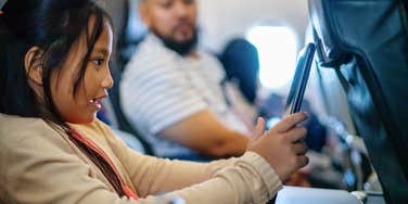 child using tablet on flight while passenger glances over