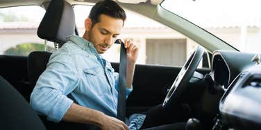 man buckling seatbelt in car while sitting behind wheel