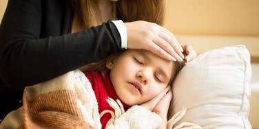 mom putting hand on the forehead of sick daughter sleeping 