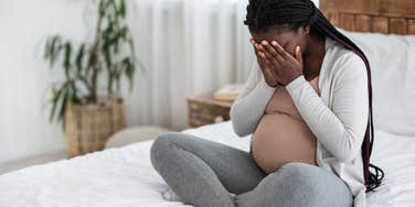 sad pregnant woman sitting on bed with head in her hands