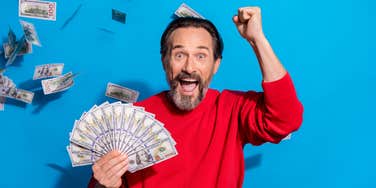 excited man holding lots of cash with more floating in the air around him