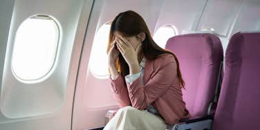 upset woman with head in hands sitting on airplane