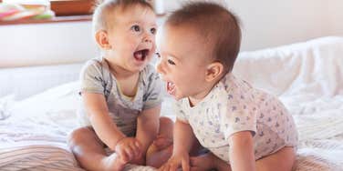 twin babies sitting on bed laughing together